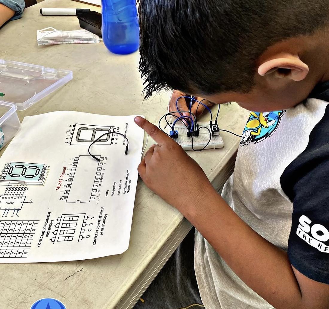 Alumno siguiendo la guía impresa del kit de robótica de CultivaTec mientras arma su circuito