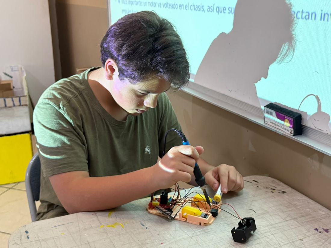 Alumno suelda los cables de un motor sobre el chasis de su robot en un taller de robótica de CultivaTec