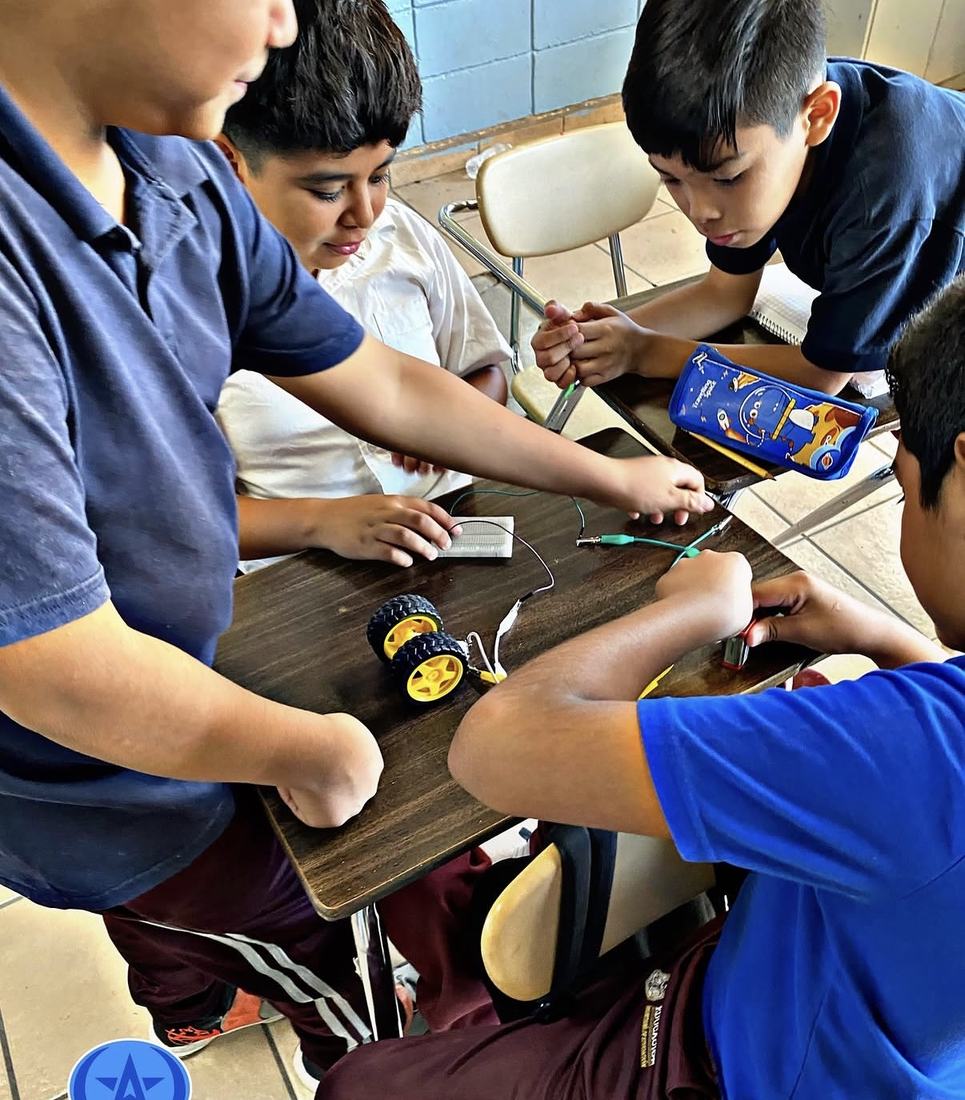 Alumnos de secundaria con uniforme trabajando con motores y ruedas en un taller de robótica en su plantel