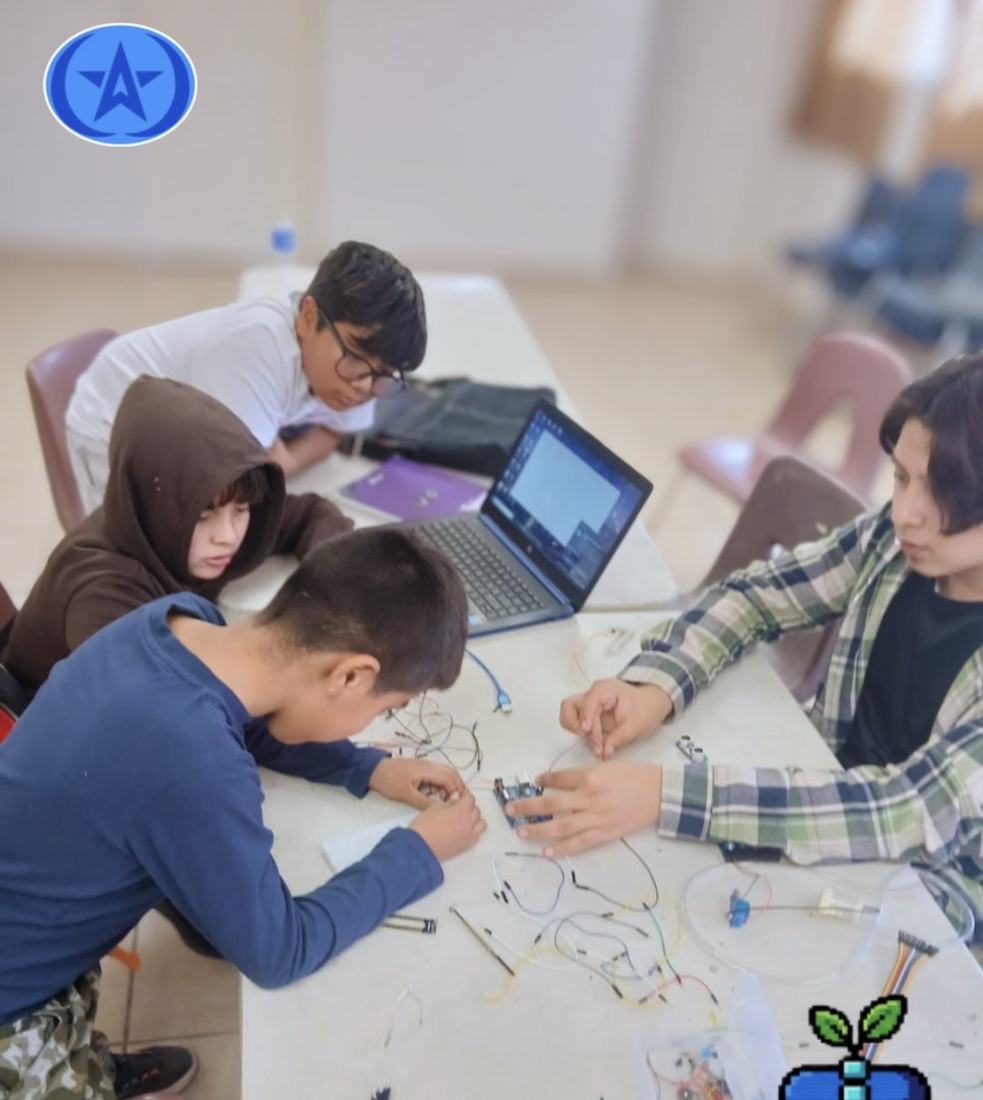 Alumnos armando circuitos alrededor de una mesa con una laptop compartida en un taller de CultivaTec