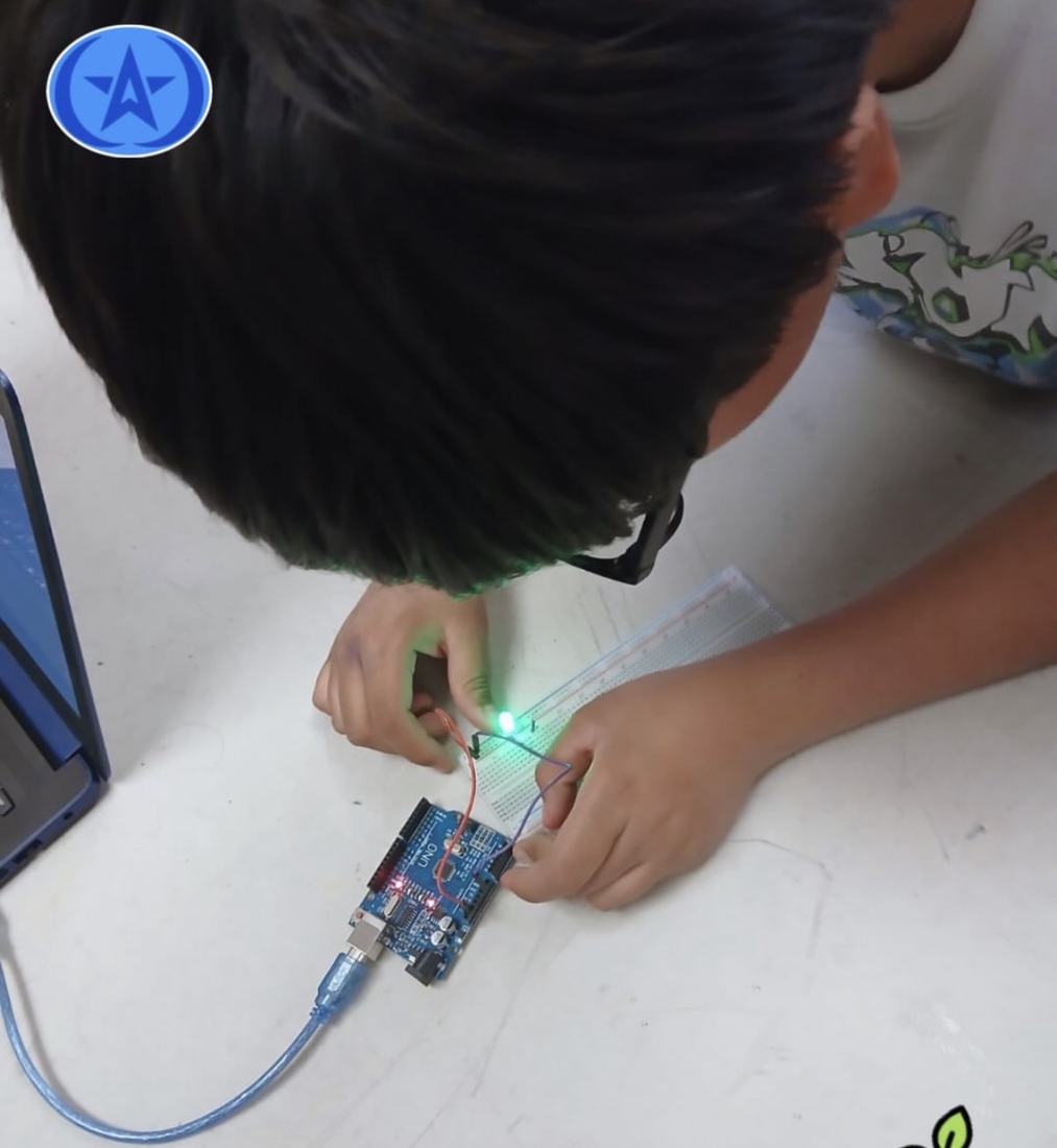 Manos de un alumno conectando una placa microcontroladora con el LED verde ya encendido