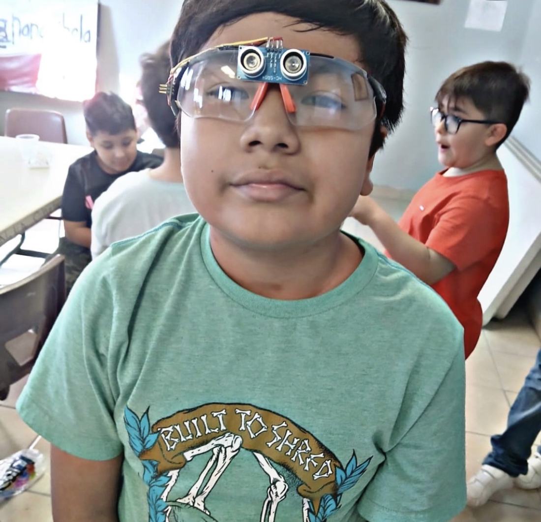 Niño con un sensor ultrasónico apoyado en la frente, jugando antes de montarlo en su robot