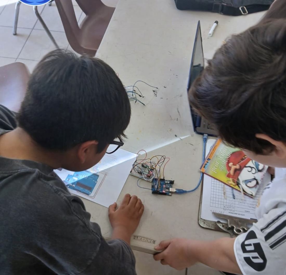 Dos alumnos trabajando en pareja: uno programa en la tablet y el otro conecta la placa del robot