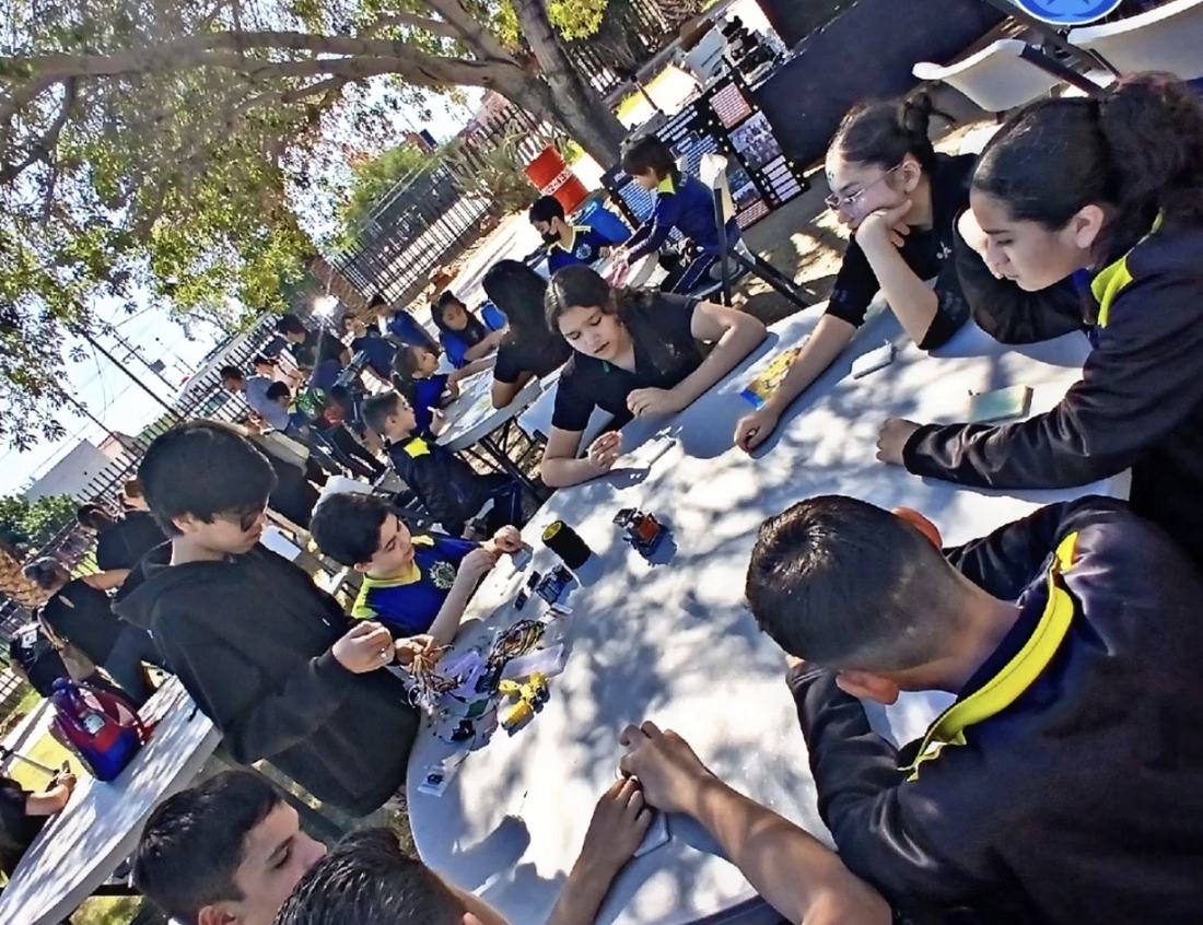 Taller gratuito de robótica de CultivaTec al aire libre, con decenas de niños trabajando en mesas bajo los árboles