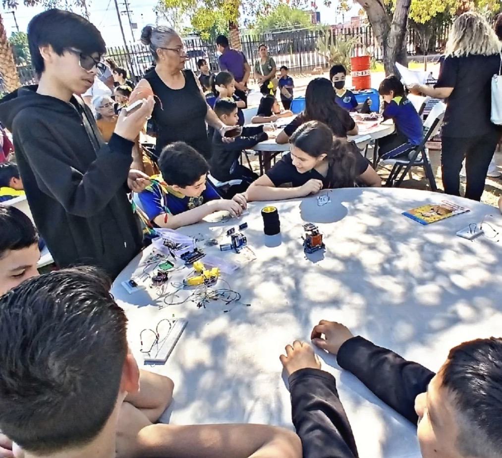 Taller comunitario de robótica de CultivaTec en un parque, con niños armando circuitos sobre una mesa redonda
